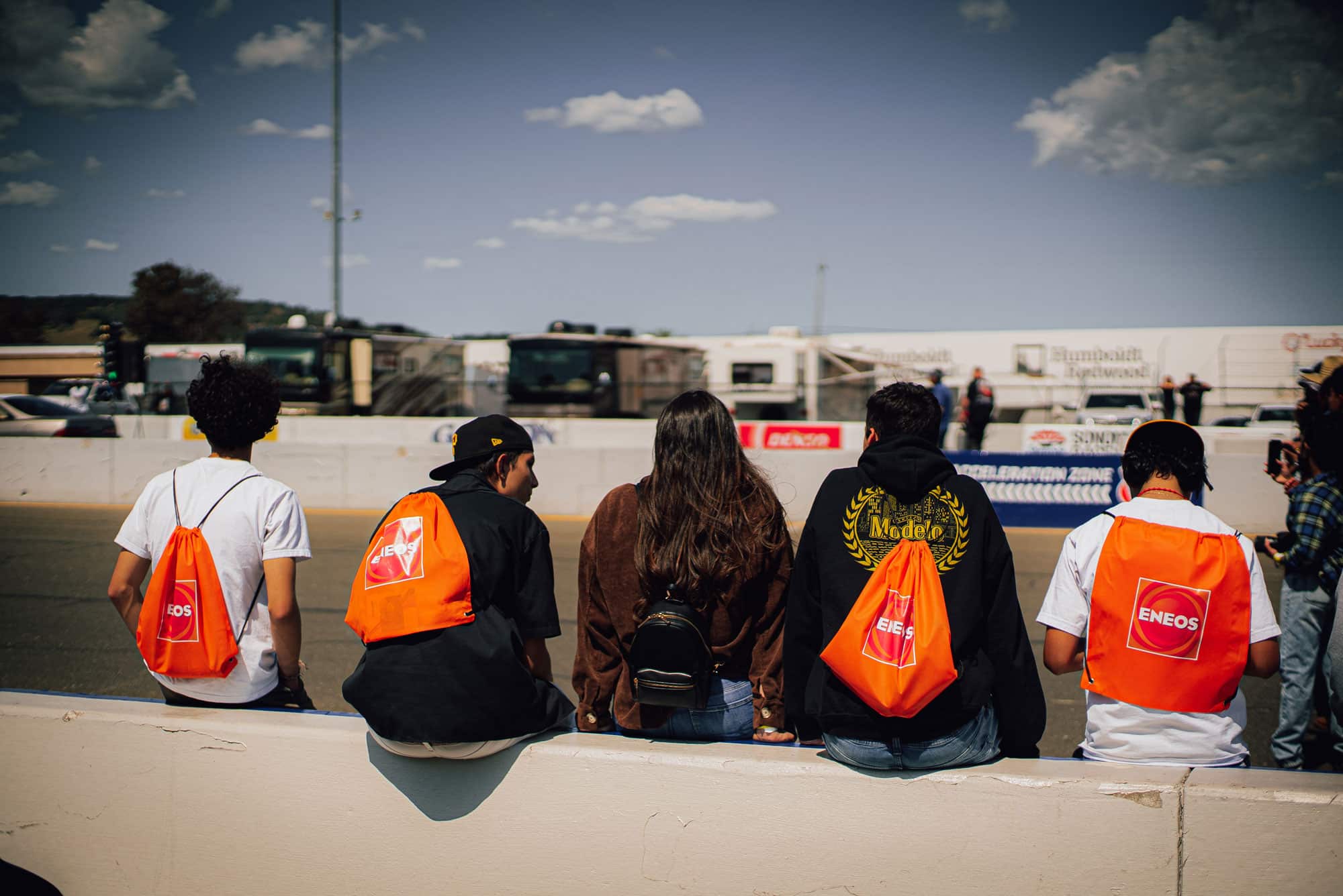 Event goers sitting on wall with ENEOS backpacks