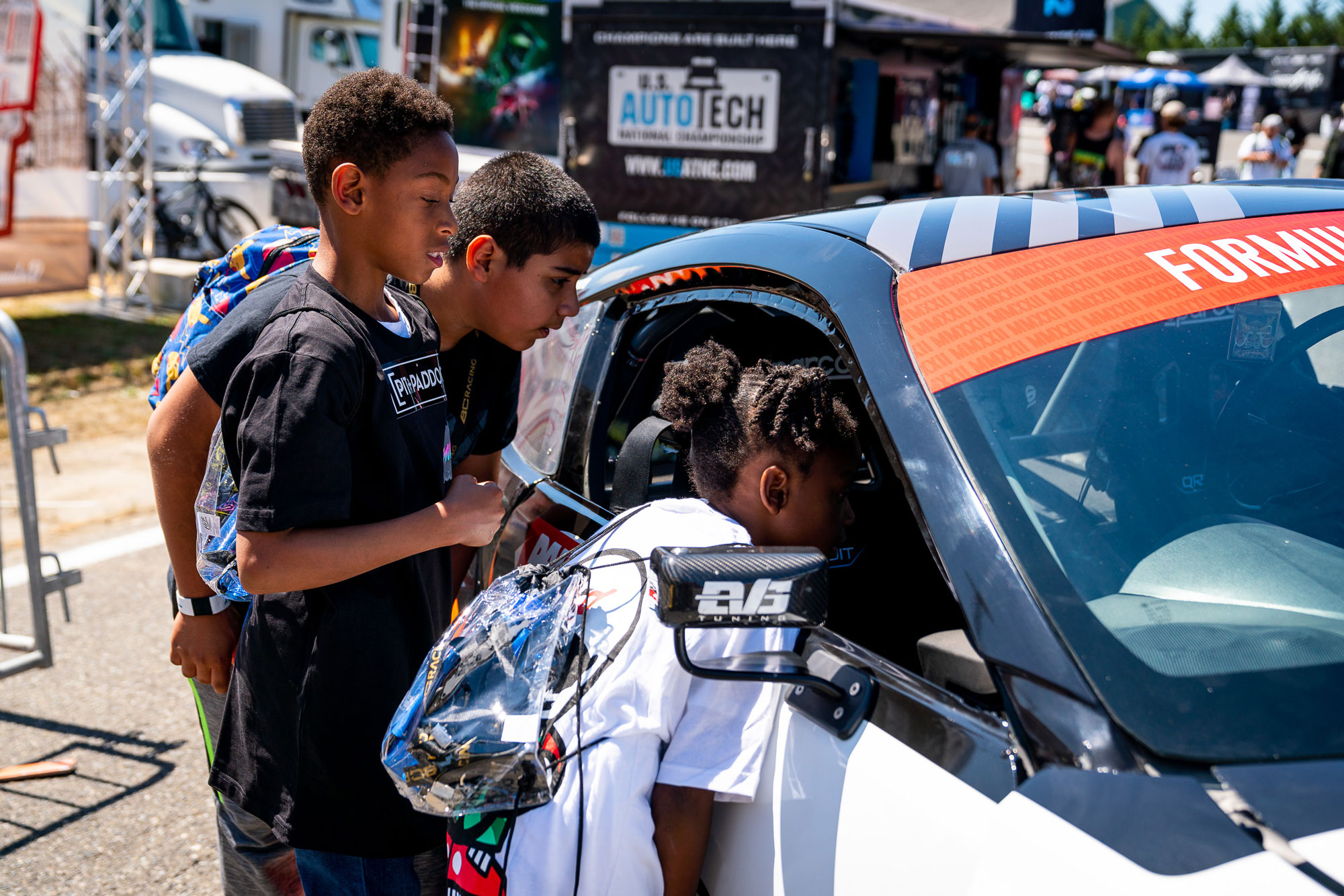 Three children looking into Pit+Paddock race car
